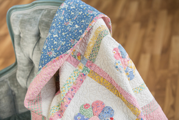 Handmade pastel quilt draped over a chair, showing soft colors, quilting texture, and careful stitching.