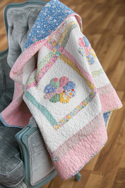 Pastel handmade quilt displayed on a chair, showing a soft color palette and detailed quilting.